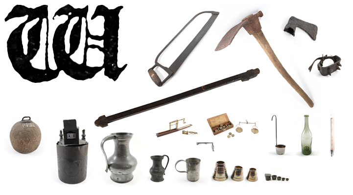 A large ornate printed capital letter W with a saw, adze, axe head, weights, measures and scales.