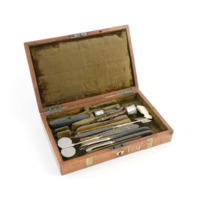 Trepanning kit. A wooden box with tools inside. The tools consist of two circular serrated cutters, a flat axe shaped tool with a serrated edge, a tool with two flat serrated discs at the end, spatulas with toothed surfaces and a brush.