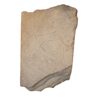 Symbol stone. A roughly rectangular slab of beige sandstone about two feet high and almost one and a half feet wide, broken at the top and bottom. Carved on the stone in simple outlines is a dog like beast with a long, curved muzzle, a mirror with a handle, a comb, and a rectangular area divided into three columns the outer two of which have a pattern of zig zagging ovals.