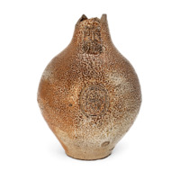 Bellarmine wine jar. A fat mottled brown ceramic bottle with a design containing a love heart stamped on the middle, and on the neck a face of a grimacing elderly bearded man with bushy eyebrows. The upper neck has broken off.