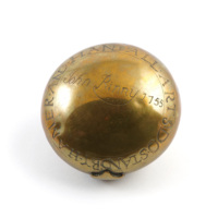 Tobacco box. A round brass box. On the bottom is the inscription John Rinny 1755 in the middle and around the edge BY HAMMER AND HAND ALL ARTS DO STAND.