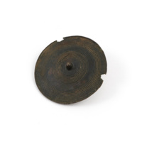 Pin head. A bronze disc about two inches wide with a knob in the centre and concentric circular depressions.