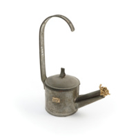 Bunker lamp. A small tin lamp shaped like a watering can, with a long handle that comes vertically up over the centre. The spout has a thick bundle of wick coming out of it.