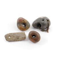 Four stones with natural holes through them, one beige and rectangular, two orange and grey, and a large grey stone with a cord through the hole.