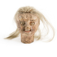 Head of Despair. A small wooden head with bared teeth, red lips and covered with flaking paint, with long white hair.