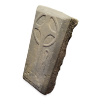 Grave slab. A large rectangular block of grey stone, about two feet tall. Carved in relief is a Celtic cross and a pair of shears.