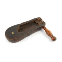 Rattle. A wooden paddle shaped block on a handle. The block has a long cavity at the bottom of which are two thin tongues of wood. These contact two wooden gears which turn and catch the tongues as the block is spun by the handle.