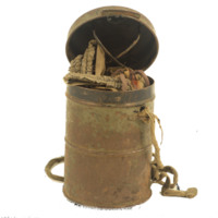 Cyclindrical cannister with faded fabric wrapped around and handle for carrying. Inside holds a fabric gas mask.