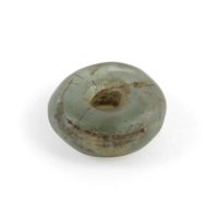 Bead. A small, fat ring shaped bead made of greenish grey glass, with scratches and scuffs.
