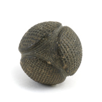 Carved stone ball. Roughly the size of a tennis ball. Black, polished stone ball with four large flat circular knobs arranged equidistant from each other. The knobs have a finely cut grid pattern and each square is rounded to produce tiny squarish knobs. The spaces between the large knobs are cut with lines that flow around the knobs.