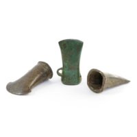Socketed axe heads. Three bronze axe heads, about three inches long, hollow inside with wide squarish openings at the base. One axe head is covered with green rust and has a loop near the base.