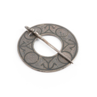 Brooch. A flat silver ring, about three inches wide, with a pin hinged onto it. The ring is decorated with incised foliage and chequered circles. The edges of the ring and circles and anchor like shapes are marked with thick blackened lines.