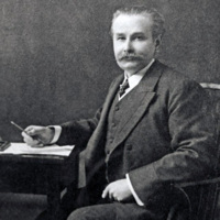 Photograph of James Mackenzie Davidson. A man with a moustache sits at a table with pen and papers. 