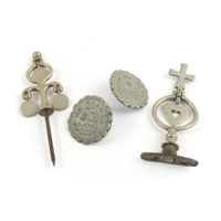 Harness ornaments. Silver coloured metal ornaments, left to right: a pin with a tree like shape and suspended discs, two circular ornaments with scalloped edges and thistle decoration, and a ring with a suspended heart and cross.