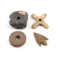Charms. Four charms, clockwise from top left: a piece of stone containing a mould for a spindle whorl, a bone cross, a ring shaped spindle whorl decorated with carved foliage, a flint arrowhead.