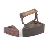 Block iron. A rounded triangular box metal box with a wooden handle and a hatch on the back, next to a similarly shaped solid block of rusty iron which fits inside. 