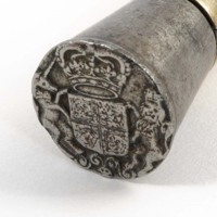 A tarnished silver cap of a staff. The cap is embossed with a coat of arms with a crown above it and a lion and unicorn on either side.
