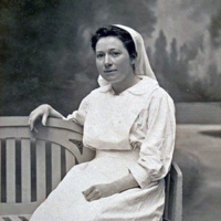 Photograph of Amelia Nyasa Laws, wearing a white nurses uniform including apron and cap. She sits on a bench with her arm around the back.