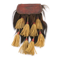 Sporran. A red leather flap with a decorative stitched border folds over a mass of brown hair hanging downwards. There are eight tassels of yellow cord arranged in two rows, also hanging downwards from the flap. 