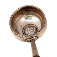 Toddy ladle. Long, turned wooden handle with a bulbous end. The silver bowl of the ladle has a coin incorporated into the bottom. The coin has the profile of a man wearing laurels and is inscribed GEORGIUS II DEI GRATIA.
