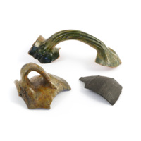 Fragments of vessels from Coull Castle. A large green ceramic handle with grooves, a fragment of brown pitted ceramic with a handle and some of the side and rim of the vessel, and a fragment of an iron cauldron.