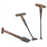 Thatching tools. A small wooden spade with two points, a metal spatula with teeth and a wooden handle, a two pronged metal fork with a wooden handle.
