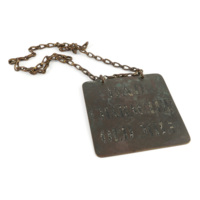Badge. A square plate of metal, about half a foot wide, with the words BAD CHARACTER OLD MILL in cracked black lettering. The reverse says DESERTER. There are two rings at the top through which runs a chain.
