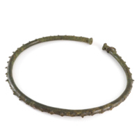 Necklet. A large bronze ring about 9 inches wide. There is an open part of the ring, and the ends have flared out terminals. Around the outer edge are numerous short projections which are the remains of smaller rings; only one of these rings is complete.