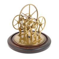 A large brass wheel sitting on four smaller wheels, in a brass frame on a circular wooden stand. The smaller wheels spin at a much slower rate when the large wheel is spun.