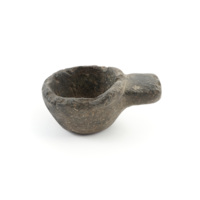 Cup. A small bowl like cup carved from a single piece of dark grey stone, with a blocky handle on one side.
