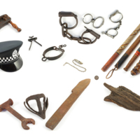A large printed capital letter P with agricultural tools, a police hat and batons, manacles, a rattle, a whistle, torture implements and a large padlock.
