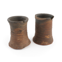 Kiln stands. Two simple cylindrical vessels of dark orange ceramic with a flared rims and bases.