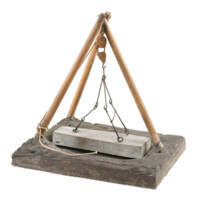 Mortsafe model. Three wooden poles arranged in a pyramid shape over a hole in the ground. Hanging over the hole is a coffin shaped slab of stone, suspended from the poles by a series of hooked metal bars and a winch.