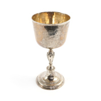 Communion cup. A slender silver cup with a tall stem. It is highly decorated with engraved scrolls, foliage and coats of arms.