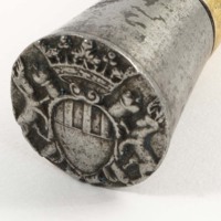 A tarnished silver cap of a staff. The cap is embossed with a coat of arms with a crown above it, crossed sceptres behind it, and a stag on either side. 