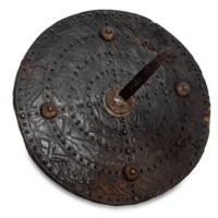Targe. A circular shield, about a foot and a half wide, covered with leather and studded with brass rivets arranged in four concentric circles. Four brass bosses incised with spiralling lines are equidistant from each other near the edge, and in the centre is a large boss with a pointed blade about a foot long projecting from it.