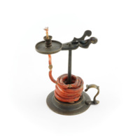 Pull up lamp. Small dark grey metal lamp. It has a circular base with a handle, and a rod projecting up from the centre. Around the rod is coiled a wick coated in a waxy red substance. The wick has been pulled through a candle holder like structure which is on top of the rod.