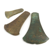 Flat axe heads. Three bronze axe heads, ranging from three to six inches long, the largest one covered in green rust.