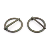 Brooches. Two small ring shaped bronze brooches with fastening pins, covered in green rust.